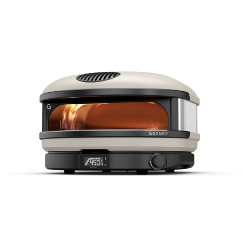 Der Gozney Arc XL Gas Pizzaofen ist ein kompakter Outdoor-Pizzaofen mit beige-schwarzer Lackierung. Mit einer digitalen Temperaturanzeige von 450 °F und einer durch die Glasfront sichtbaren Flamme bietet dieser Kompaktofen Platz für 16-Zoll-Pizzen. Der Markenname „Gozney“ ist deutlich auf der unteren Frontplatte zu sehen.
