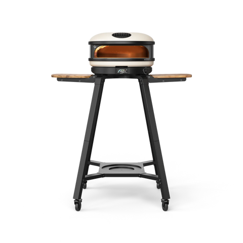 Das Gozney ARC und ARC XL Gestell ist ein moderner Outdoor-Pizzaofen auf Rädern, der mit klappbaren Holzseitentischen und einem stabilen schwarzen Ständer mit Ablagefläche ausgestattet ist. Sein Metallofen verfügt über eine runde Edelstahl-Backkammer und einen sichtbaren Bedienknopf an der Vorderseite, der sowohl Funktionalität als auch leichte Manövrierbarkeit gewährleistet.