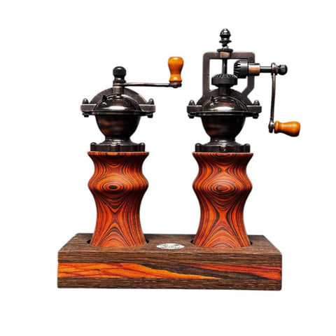 Ein manuelles Pfeffermühlen- und Salzmühlen-Set im Vintage-Stil von Jungo Design mit Holzsockeln, Metallgriffen und dunkler, wirbelnder Holzmaserung. Beide sind auf einer gemeinsamen Coccobollo-Plattform montiert und unterstreichen so die Nachhaltigkeit bei jedem Gebrauch.