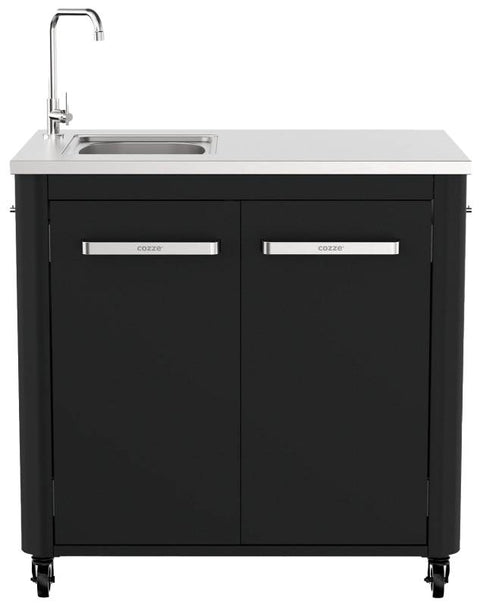 Die Cozze Aussenküche 90 besticht durch einen eleganten, schwarzen Standschrank mit silbernen Griffen und harmoniert perfekt mit der Edelstahlspüle und dem Wasserhahn auf der weißen Arbeitsplatte. Entwickelt für Außenküchen, ermöglichen die Räder eine einfache Mobilität für verschiedene Grillstationen.
