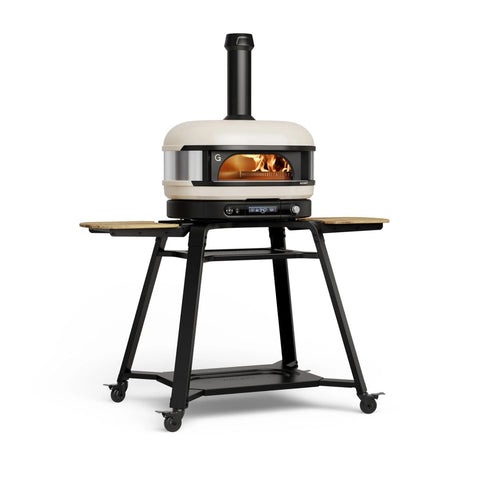 Der Gozney Dome Gen 2 Pizzaofen - Hybrid Brennstoffsystem von Gozney verfügt über eine cremefarbene Kuppel, ein gläsernes Feuerfenster, einen Schornstein und klappbare Ablagen - ideal für Ihre Outdoor-Küche - auf einem schwarzen Rollständer mit unterem Ablagefach.
