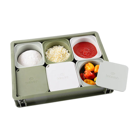 Eine rechteckige Babadoh-Box – Olive mit sechs Fächern enthält verschiedene Lebensmittel. Die obere Reihe enthält Mehl, geriebenen Käse und Tomatensoße – perfekt als Zubehör für jeden Pizza-Liebhaber. Die untere Reihe enthält abgedeckte Behälter, von denen einer offen ist und Kirschtomaten freigibt. Diese lebensmittelsichere Schale und ihre Deckel sind grün und weiß.