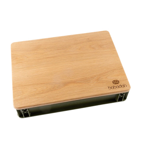 Un tagliere rettangolare in legno con bordi arrotondati e il logo "Babobah" nell'angolo in basso a destra. Questa confezione di Babadoh (6 contenitori, cassetta per le olive e tagliere in legno di quercia) poggia su una base che la solleva leggermente ed è dotata di vani portaoggetti sottostanti.