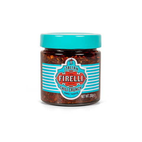 Ein transparentes Glas mit Casa Firelli Chili Crunch präsentiert den dunkelroten, strukturierten Inhalt dieses würzigen Gewürzes. Das mit einem türkisfarbenen Deckel versehene Etikett zeigt rote und türkisfarbene Streifen mit dem Text „Chili Crunch 200 g“, was darauf hinweist, dass es aus kalabrischen Chilis hergestellt wird.