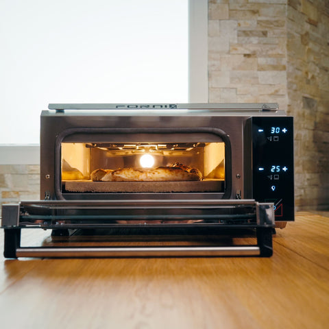 Ein Effeuno Pizzaofen P134H PRO 509°C mit Digitalanzeige backt eine köstliche Pizza. Die Ofentür ist geöffnet und präsentiert die ansprechende Pizzaqualität. Eine Steinmauer und ein Fenster bilden eine charmante Kulisse.