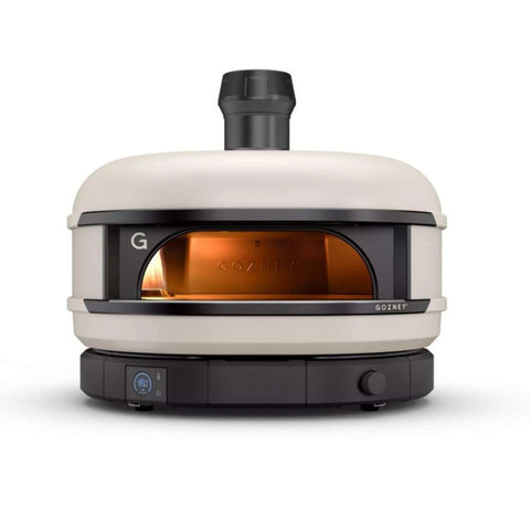 Ein moderner, beigefarbener Gozney Dome S1 Gas-Pizzaofen mit großer Öffnung zum Einschieben von Pizzas. Der Ofen sitzt auf einem schwarzen Sockel mit einem digitalen Bedienfeld und einem Drehschalter auf der Vorderseite. Oben in der Mitte ist ein schwarzer Kamin angebracht, der Restaurantqualität nach Hause bringt. Der Innenraum wird mit einem orangefarbenen Schein beleuchtet.