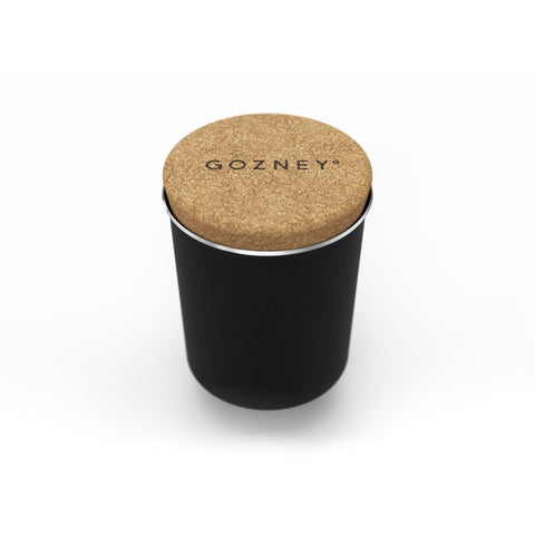 Ein schwarzer zylindrischer Behälter mit einem Korkdeckel trägt die Aufschrift „Gozney“. Der als Gozney Steamer / Dampfinjektor für Dome für Brotbacken-Enthusiasten konzipierte Behälter verfügt über eine glatte, matte Oberfläche und einen silbernen Rand an der Oberseite. Der Hintergrund ist schlicht weiß.
