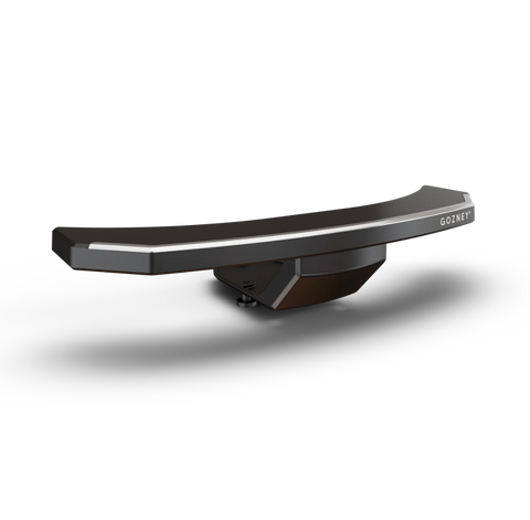 Eine schlanke, schwarze, gebogene, moderne TV-Soundbar vor einem schwarzen Hintergrund. Die Soundbar hat an ihrer Oberkante eine silberne Einfassung, die an keramikbeschichteten Edelstahl erinnert, und am rechten Ende ist der Markenname „Gozney“ zu sehen. Das Design ist minimalistisch und geradlinig.