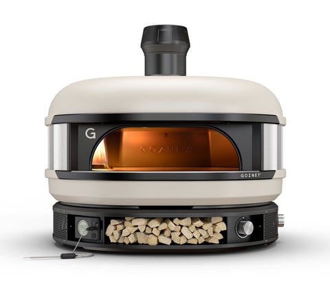 Ein Gozney Dome Pizzaofen (Multi-Fuel Gas/Holz) mit weißer Außenseite und schwarzem Rand. Der Ofen hat einen zentralen Kamin, eine Glasfront und darunter ein Fach, das mit Holzscheiten gefüllt ist. Ein an der Seite angebrachtes digitales Thermometer ermöglicht eine präzise Temperaturregelung, sodass er für jeden Benutzer einfach zu bedienen ist.