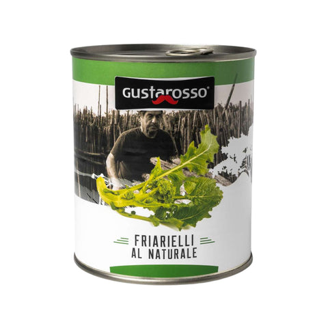 Une boîte cylindrique avec une étiquette verte et blanche montre clairement le nom de la marque "Gustarosso" avec un logo en forme de moustache. En dessous, une image de légumes-feuilles et d'une personne en arrière-plan met en évidence "Friarielli al naturale" et présente des brocolis napolitains naturels, indispensables dans la cuisine méditerranéenne. Le produit Gustarosso Friarelli Brocoli (700 g) est clairement indiqué sur l'emballage.