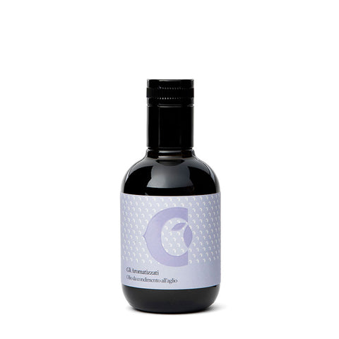 Une bouteille en verre foncé avec un bouchon noir et une étiquette violet clair au design abstrait, dont un croissant stylisé et une gousse d'ail, porte le texte : "Gli Aromatizzati Olio condimento all'aglio". Cette bouteille de 100 ml d'"huile d'olive extra vierge aromatisée à l'ail" de Ciccolella propose une huile d'olive extra vierge aromatisée à l'ail.