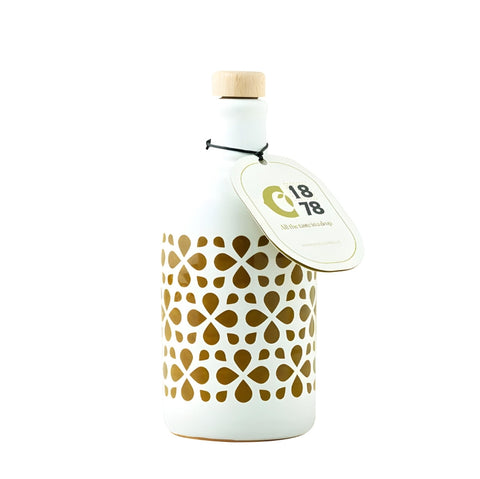 Une huile d'olive extra vierge ORCIO Keramik Intensità (250 ml) de Ciccolella est présentée dans une bouteille en céramique blanche, décorée d'un bouchon en bois et d'une cordelette noire qui sécurise l'étiquette. La bouteille présente un élégant motif floral doré et porte une étiquette ronde avec l'inscription "C18 78" et un texte supplémentaire. Elle convient parfaitement à la conservation de l'huile d'olive extra vierge et se détache gracieusement sur un fond blanc sobre.