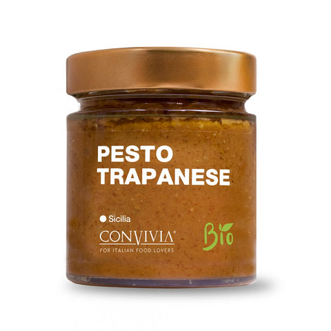 Ein Glas Bio Trapani Pesto Convivia mit goldenem Schraubdeckel. Das Etikett zeigt den Text „Pesto Trapanese, Sicilia, Bio“ und „Convivia, für Liebhaber italienischer Küche“ auf weißem Hintergrund. Das Glas enthält eine rotbraune Soße, die aus getrockneten Tomaten und nativem Olivenöl extra hergestellt wird.