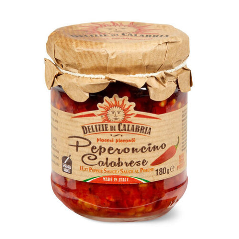 Ein Glas mit Delizie di Calabria Gehackter Chili (Peperoncino Calabrese) in Öl Delizie di Calabria. Das Glas ist mit einer braunen Papierhülle versehen, die mit einer Schnur befestigt ist, und hat ein Etikett mit einer Abbildung einer Chili aus Kalabrien und dem Produktnamen. Das Glas enthält 180 Gramm Soße.