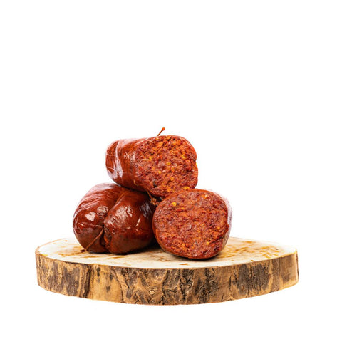 Tre pezzi di salsiccia cruda sono impilati su una tavola di legno. Due pezzi sono interi, mentre uno è aperto per rivelare un interno ruvido e rossastro, punteggiato di spezie. Questa specialità salata dimostra la produzione tradizionale che rende così particolare la Madeo Nduja di Spilinga in budello piccante (250 g). Lo sfondo è bianco.