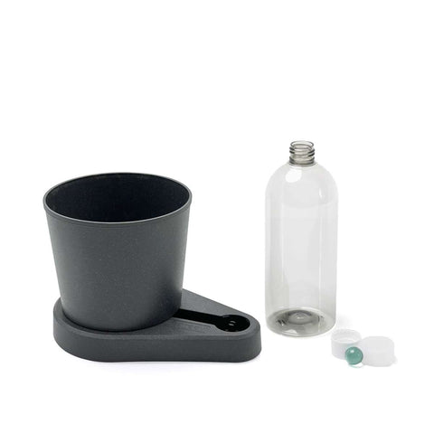 Bild eines grauen selbstbewässernden Blumentopfs mit befestigtem Sockel, perfekt für den Anbau von Küchenkräutern, neben einer transparenten leeren Wasserflasche mit Deckel und einer blauen Kugel. Der greevi Kräuterheld selbstbewässernder Kräuter-Pflanztopf (GREEVI) von Grevi verwendet ein patentiertes Bewässerungssystem, um den Bewässerungsprozess zu automatisieren und so ein konstantes Feuchtigkeitsniveau zu gewährleisten.
