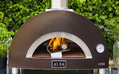 Der Alfa Forni Moderno One Holz-Pizzaofen ist ein Pizzaofen aus Edelstahl für den Außenbereich, der sich mit seinem sichtbaren Feuer ideal für die Zubereitung authentischer neapolitanischer Pizza eignet. Dieser vielseitige Alfa Forni-Ofen verfügt über eine Temperaturanzeige und wird vor üppigem grünem Laub in Szene gesetzt.