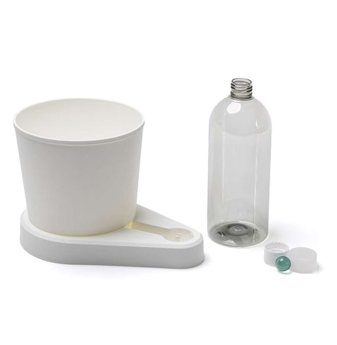 Ein weißer Plastikbecher steht auf einem passenden Untersatz mit Halter. Neben dem Untersatz steht eine klare Glasflasche ohne Deckel. Neben der Flasche befinden sich ein Plastikdeckel und eine grüne Murmel, beide separat platziert – ideal zum Aufbewahren frischer Kräuter. Die Objekte sind auf einem weißen Hintergrund positioniert und bilden den greevi Kräuterheld selbstbewässernder Kräuter-Pflanztopf (GREEVI) von Grevi.