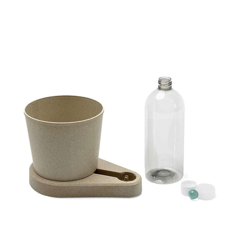 Ein beigefarbener Pflanztopf und eine Tropfschale werden neben einer durchsichtigen Plastikflasche mit breiter Öffnung ausgestellt. Die Flasche mit ihrem weißen Deckel und der kleinen grünen Kugel erinnert an einen Grevi greevi Kräuterheld selbstbewässernder Kräuter-Pflanztopf. Diese Gegenstände deuten auf Funktionalität hin, wahrscheinlich im Zusammenhang mit der Pflanzenpflege oder der Bewässerung Ihrer frischen Kräuter.