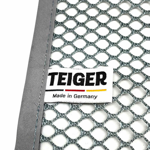 Nahaufnahme eines Netzmaterials mit grauem Rand und einem weißen Stoffetikett. Auf dem Etikett steht in fetten schwarzen Buchstaben „Teiger Teigreinigungstuch (Doppelpack)“, darunter die Farben der deutschen Flagge und darunter „Made in Germany“. Es ist ideal zum Reinigen von Backutensilien und entfernt mühelos Teigrückstände. Präsentiert von Pizzalovers.