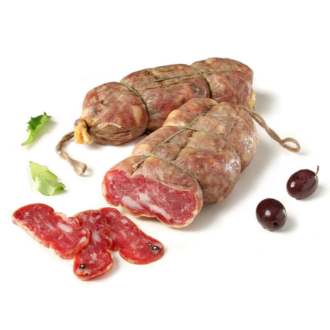 Deux gros morceaux de salami Madeo Soppressata BIO (doux) sont posés sur une surface blanche, attachés par des ficelles, devant lesquels trois tranches de salami sont découpées et exposées. À côté du salami se trouvent deux olives noires et quelques feuilles vertes.