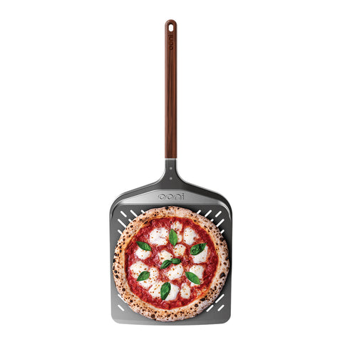Eine frisch gebackene Pizza mit Mozzarella, Tomatensoße und Basilikum ruht auf dem Ooni Pizzaschieber Signature Perforiert 12" von Ooni vor einem weißen Hintergrund.