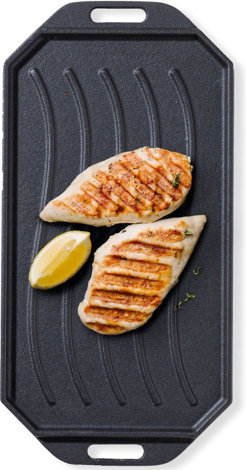 Zwei gegrillte Hähnchenbrüste mit Grillspuren und einer Zitronenspalte werden auf der Cozze Gusseisen-Wendepfanne mit Untersetzer 165x330mm von Cozze serviert, die mit geriffelten Linien versehen ist.