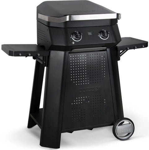 Ein schwarzer Cozze-Gasgrill mit geschlossenem Deckel, zwei Knöpfen, seitlichen Ablagen, Rädern und belüfteter Frontplatte - ideal zur Kombination mit Ihrem Cozze Outdoor-Tisch für E-500 Elektrogrill, G-500 Gasgrill und Plancha.