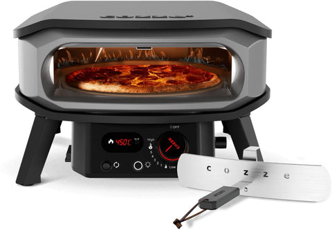 Der Cozze 13 inch Pizzaofen PREMIUM ROTATE von Cozze backt mit rotierendem Stein und 450°C köstliche Pepperoni-Pizza, während Flammen lodern; davor liegt ein silberner, mit "COZZE" beschrifteter Pizzaschieber.