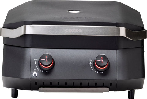 Der Cozze G-500 Grill, Gas 50mbar - CH-Regler bietet ein kompaktes, schwarzes Tischgerät mit Edelstahlgriff, zwei roten Bedienknöpfen und Lüftungsschlitzen. Das "cozze" Logo ist auf Griff und Deckel sichtbar - ideal für deine Terrassenküche.