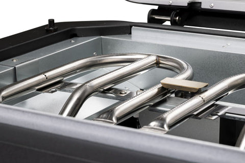 Nahaufnahme der Brennerrohre aus Edelstahl und des Keramikzünders im Inneren des Cozze G-500 Grill, Gas 50mbar - CH-Regler von Cozze, die Teile des Innenraums und des Deckels des kompakten Grills zeigen - ideal für jede Gasgrillterrasse.