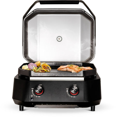 Der Cozze G-500 Plancha mit Deckel von Cozze grillt Lachs, Paprika, Zucchini und rote Zwiebeln auf einer flachen Gusseisen-Grillplatte. Zwei Bedienknöpfe sind an der Vorderseite platziert.