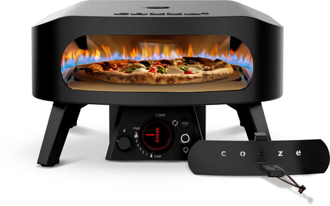 Ein Cozze Pizzaofen Rotate - Black Edition [13 Zoll], Gas, 50mbar - CH-Regler kocht Pizza mit einer sichtbaren Gasflamme und Bedienelementen an der Vorderseite. Daneben steht ein Cozze 13 Zoll Rotate Pizzaschieber, der mit seinem rotierenden Pizzastein für gleichmäßige Backergebnisse sorgt.