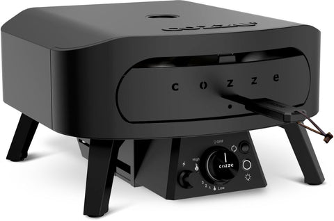 Der Cozze Pizzaofen Rotate - Black Edition [13 Zoll], Gas, 50mbar mit Frontöffnung, Bedienknöpfen und Temperaturanzeige steht auf vier Beinen, während eine Pizzaschaufel hineingeschoben wird, bereit zum Backen auf dem rotierenden Stein.