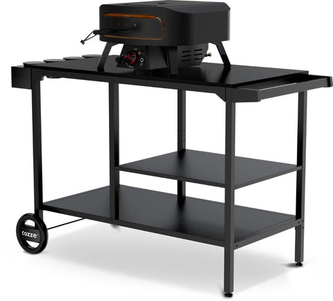 Die Cozze Elements BBQ Station von Cozze verfügt über einen schwarzen Metallrahmen, zwei Ablagen, eine Edelstahl-Arbeitsfläche und Räder an einem Ende. Ein kompakter, moderner Pizzaofen befindet sich auf dieser eleganten Outdoor-Kücheneinrichtung.