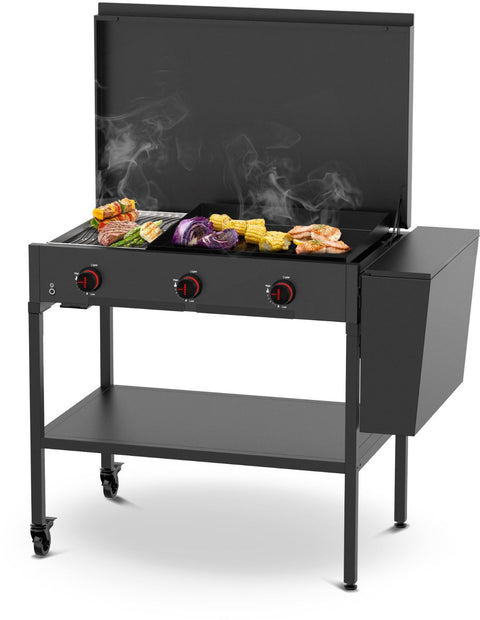 Ein schwarzer Outdoor-Gasgrill mit drei roten Bedienknöpfen, einem Seitenfach und Rädern grillt Gemüse und Fleisch, während der Rauch aufsteigt - ideal in Kombination mit den Outdoor-Küchen-Modulen von Cozze wie dem Cozze Elements Abfalleimer.