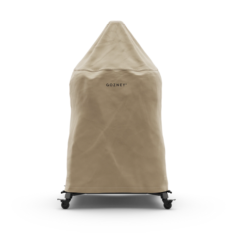 Eine beige Gozney Abdeckhaube für Dome 2.0 / Dome 2.0 XL Lang ist als wetterfester Schutz über einen auf Rollen stehenden Outdoor-Ofen von Gozney gezogen und vor weißem Hintergrund zu sehen.
