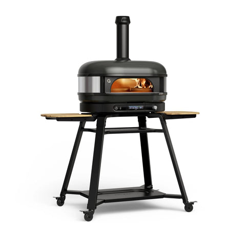 Der Gozney Dome Gen 2 XL Pizzaofen von Gozney hat ein elegantes schwarzes Design mit Schornstein, Glasfront, sichtbaren Flammen und einem Hybrid-Brennstoffsystem. Er steht auf einem fahrbaren Metallsockel mit klappbaren Seitenablagen aus Holz - ideal für Pizzaliebhaber.