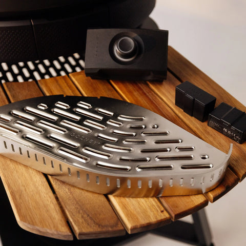 Ein Gozney Holzfeuer Control-Kit für Dome (Gen 2) / Dome XL (Gen 2), bestehend aus einer Grillplatte aus Edelstahl, zwei schwarzen Batterien und einem elektronischen Gerät, steht auf einem runden Holzlattentisch.