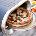 Eine frisch gebackene Pizza wird mit einem Metall-Pizzaschieber aus dem Revolve Gas Pizzaofen mit rotierendem Stein von Revolve gezogen.