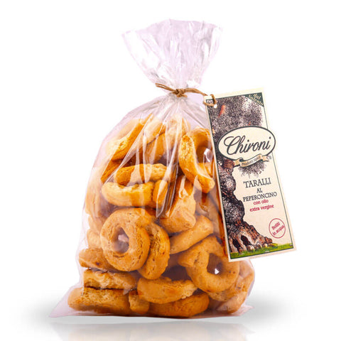 Ein durchsichtiger Plastikbeutel, gefüllt mit runden, goldbraunen Taralli-Snacks. Auf dem Etikett des Beutels ist ein Olivenbaum abgebildet und das Logo trägt den Schriftzug „Chironi“. Auf dem Etikett steht auch „Taralli mit Chilischote 250 g“ auf Deutsch, was das apulische Snack-Erlebnis perfekt macht.