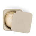 Ein runder Teigball, bekannt als Pizzateigbälle, wird leicht mit Mehl bestäubt und in einen beigefarbenen, quadratischen Behälter gelegt. Der teilweise abgedeckte Deckel trägt den geprägten Text „babadoh“ zusammen mit einem Logo, ideal für Ihre nächste Pizzazubereitung. Wir präsentieren den Babadoh Silikon Pizzateig- und Zutatenbehälter – Einzelstück von Babadoh.