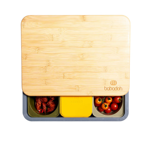 Ein rechteckiger Bambusdeckel mit der Gravur „Babadah“ bedeckt teilweise die Babadoh Box – Steel von Babadoh, unterteilt in drei Abschnitte zur Aufbewahrung von Chicken Wings, einer Box mit gelbem Deckel und Kirschtomaten – ideal für Pizza-Liebhaber bei jedem Teig-Abenteuer.
