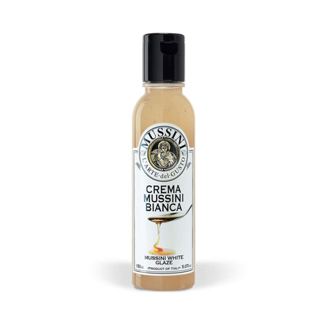 Eine 150-ml-Flasche von Mussinis Crema Balsamica - Crema Gourmet Weiss hat einen schwarzen Verschluss und ein Etikett mit einer Glasurgrafik und „Arte del Gusto“. Diese italienische weiße Balsamico-Creme bietet ein süß-saures Aroma aus erstklassigem Traubenmost.