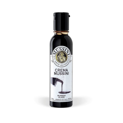 Eine Flasche Crema Balsamica - Gourmet Klassisch 150 ml von Mussini hat einen schwarzen Verschluss, auf dem Etikett ist das Mussini-Markenlogo und ein Bild einer gegossenen Glasur zu sehen, das die Gourmetqualität hervorhebt. Die Flasche wird geschmackvoll vor einem schlichten weißen Hintergrund präsentiert.