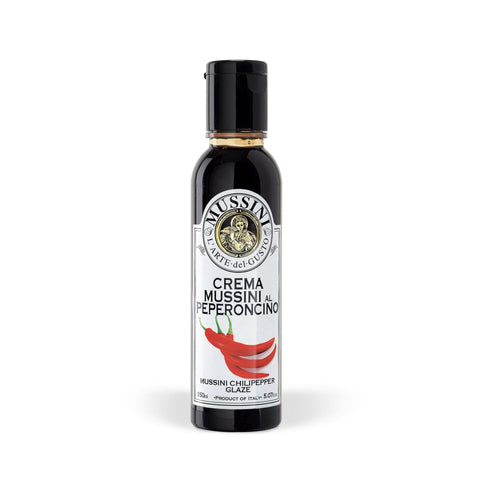 Eine Flasche Crema Balsamica - Crema Peperoncino Chiliglasur 150 ml von Mussini mit schwarzem Deckel und einem Etikett mit Abbildungen von roten Chilischoten. Diese Gourmetglasur wird in Italien aus Balsamico-Essig aus Modena hergestellt und verleiht ihr eine authentische Note.