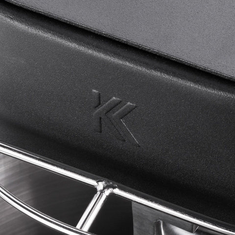 Nahaufnahme der schwarzen Metalloberfläche der KernKraft KnetKraft 5 Spiral-Knetmaschine mit geprägtem "K"-Logo und einem glänzenden, gebogenen Drahtgestell - Markenzeichen dieser hochwertigen Knetmaschine für perfekten Pizzateig. Der Deckel ist glatt und stabil.