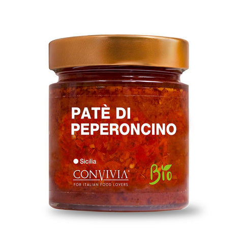 Ein Glas mit einem metallisch goldenen Deckel und der Aufschrift „Bio-Chilipastete Convivia“ enthält eine feurige Schärfe-Pastete aus roten Chilischoten. Auf dem Etikett sind der Markenname „CONVIVIA“, die Worte „Für Liebhaber italienischer Küche“, ein „Bio“-Emblem und „Sicilia“ zu sehen, was auf die Herkunft der Bio-Chilis hinweist.