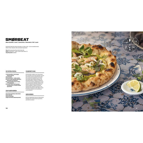 Eine Gourmet-Pizza mit Garnelen, Grünzeug und Zitrone liegt auf einer blau gemusterten Tischdecke neben einer Zitronenspalte; links daneben liegt "In Pizza We Crust - Das Buch für alle, die Pizza lieben" aus der Ava Verlagsauslieferung aufgeschlagen mit Pizzarezepten in deutscher Sprache.
