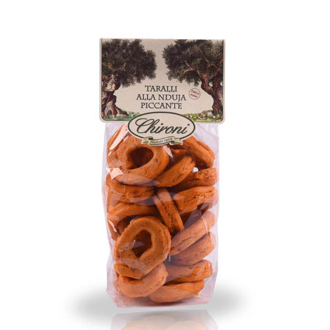 Eine durchsichtige Plastikverpackung mit ringförmigen Snacks mit der Aufschrift „Taralli mit Nduja (Scharf) 200 g“. Auf der Oberseite der Tüte sind zwei Olivenbäume abgebildet und der Markenname „Chironi“, der die wahre apulische Tradition verkörpert. Die Taralli scheinen mit scharfer Nduja gewürzt zu sein.